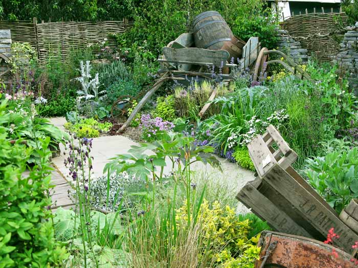 Photo of a garden with a muted mainly green planting with wooden crates and an old cart