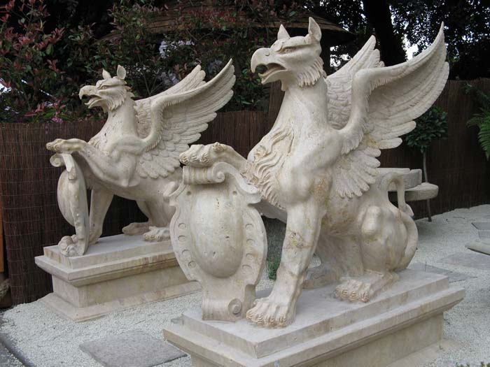 A photo of 2 garden statues with the body of a lion and the wings and head of an eagle.
