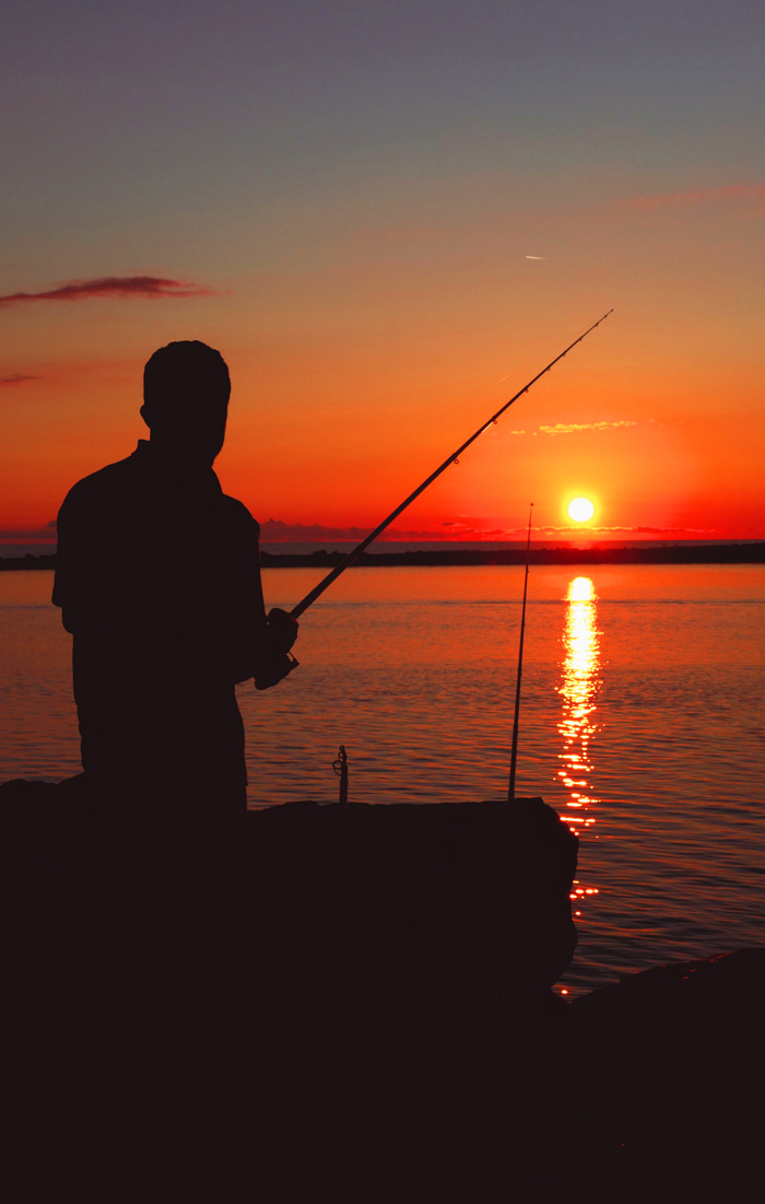 Photo of a lone fisherman at sunset holding his rod against a setting sun